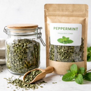 Dried peppermint leaves displayed in a glass apothecary jar and kraft pouch with wooden scoop on a white kitchen background.