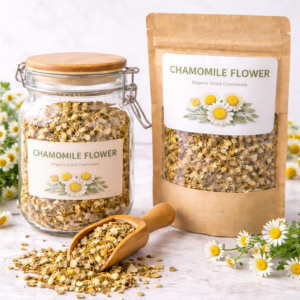 Organic dried chamomile flowers displayed in a glass jar and kraft pouch with wooden scoop on a white apothecary background.