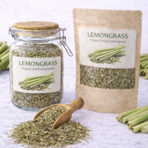 Organic dried lemongrass in a glass jar and kraft resealable pouch with wooden scoop spilling loose cut lemongrass on marble surface, fresh lemongrass stalks arranged around packaging.