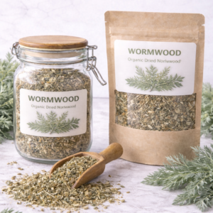 Glass jar and kraft paper pouch filled with organic dried wormwood herb on a light marble surface, wooden scoop spilling loose wormwood leaves with fresh silvery-green sprigs arranged around the packaging.