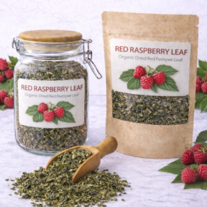 Organic dried red raspberry leaf in a glass jar and kraft pouch with wooden scoop spilling loose herb on marble surface, fresh raspberries placed around packaging.