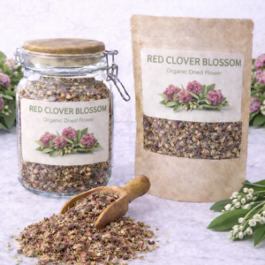 Organic dried red clover blossom in a glass jar and kraft resealable pouch with wooden scoop spilling loose dried blossoms on marble surface, fresh pink red clover flowers and green leaves arranged around packaging.