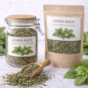 Clear glass jar and kraft paper pouch filled with organic dried lemon balm leaves, surrounded by fresh green lemon balm sprigs and a wooden scoop spilling loose leaves on a marble surface.