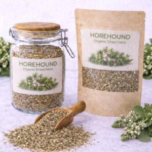 Organic dried horehound herb in a glass jar and kraft resealable pouch with wooden scoop spilling loose cut horehound on marble surface, fresh horehound sprigs with small white flowers arranged around packaging.